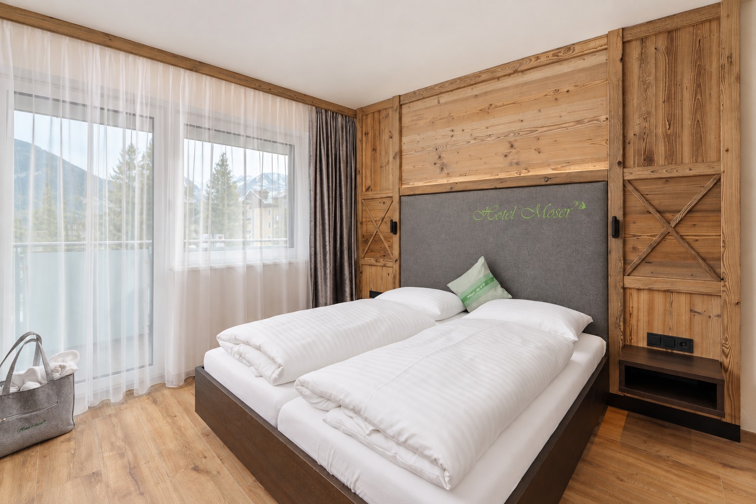 Hotelzimmer mit warmen Holzflächen, hellen Gardinen und grauen Vorhängen